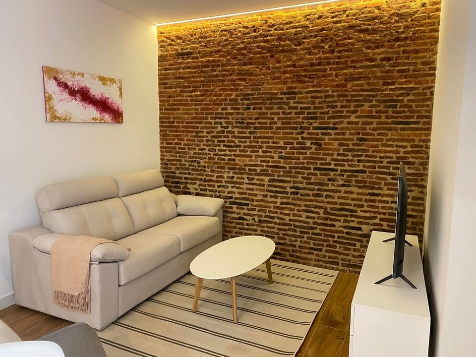 Salón reformado con pared de ladrillo visto, obra real de Ingeniería Estudios y Reformas